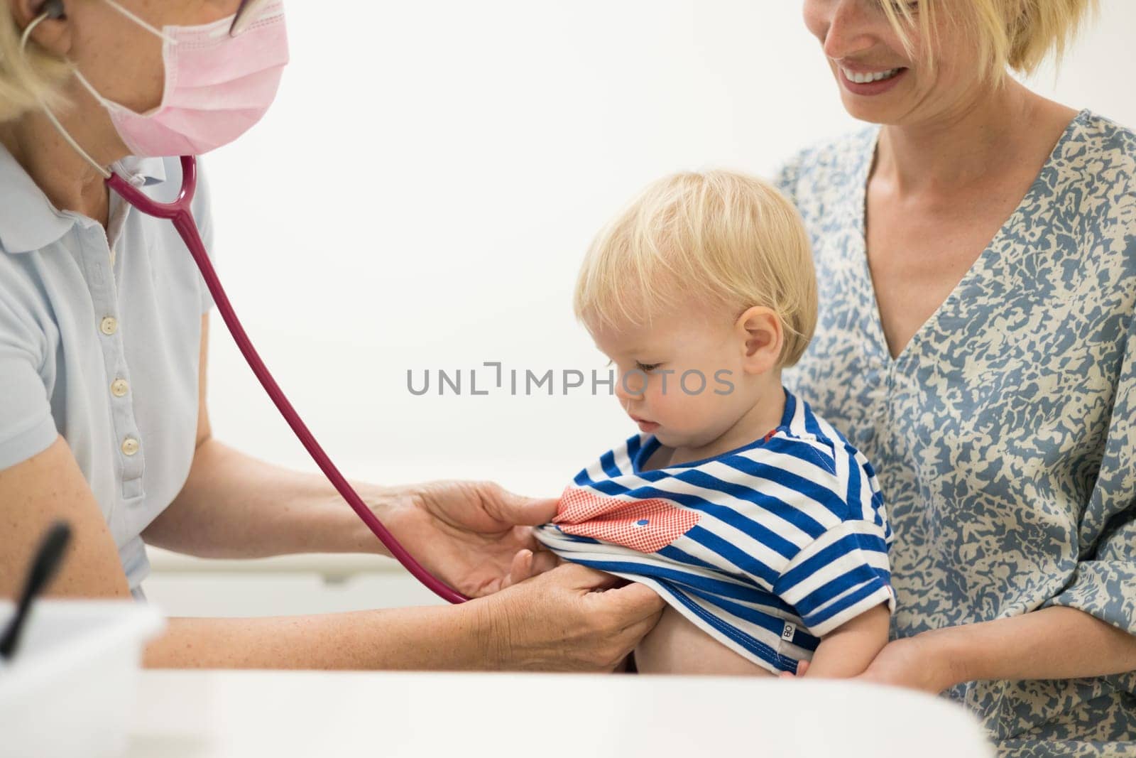 Infant baby boy child being examined by his pediatrician doctor during a standard medical checkup in presence and comfort of his mother. National public health and childs care care koncept