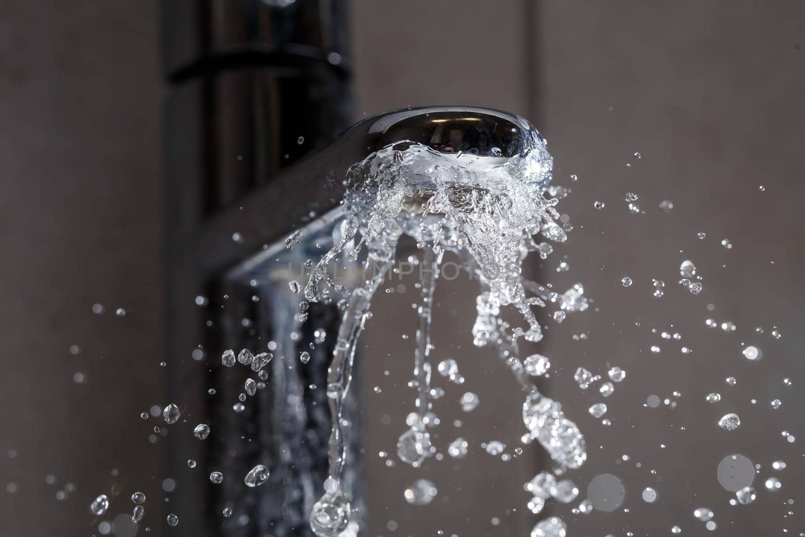 Broken water faucet in the bathroom sink. Water splashes from the silver faucet. Selective focus