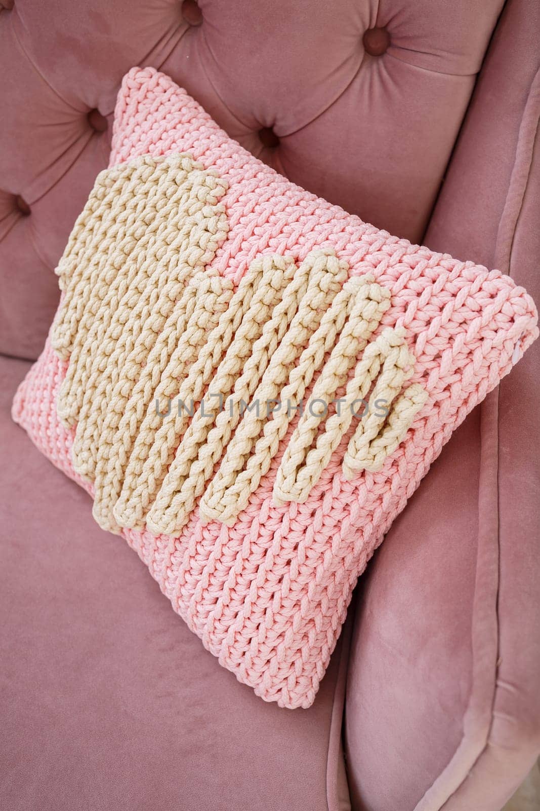 Knitted handmade pillow with pink threads lies on the sofa.