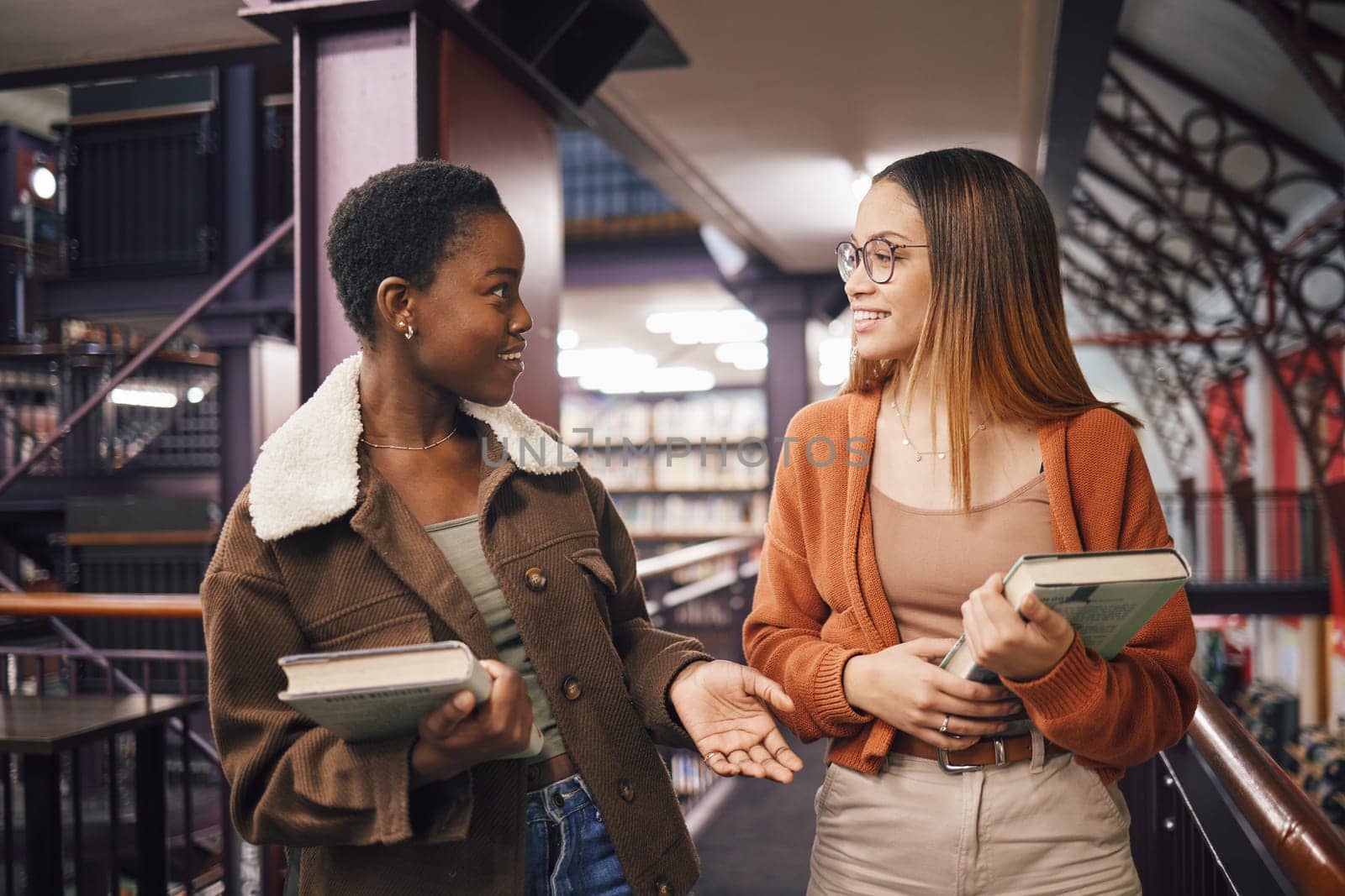 University students, library and talking about books, education and learning together at campus. Women friends have conversation about knowledge, studying and walking to research studying scholarship by YuriArcurs