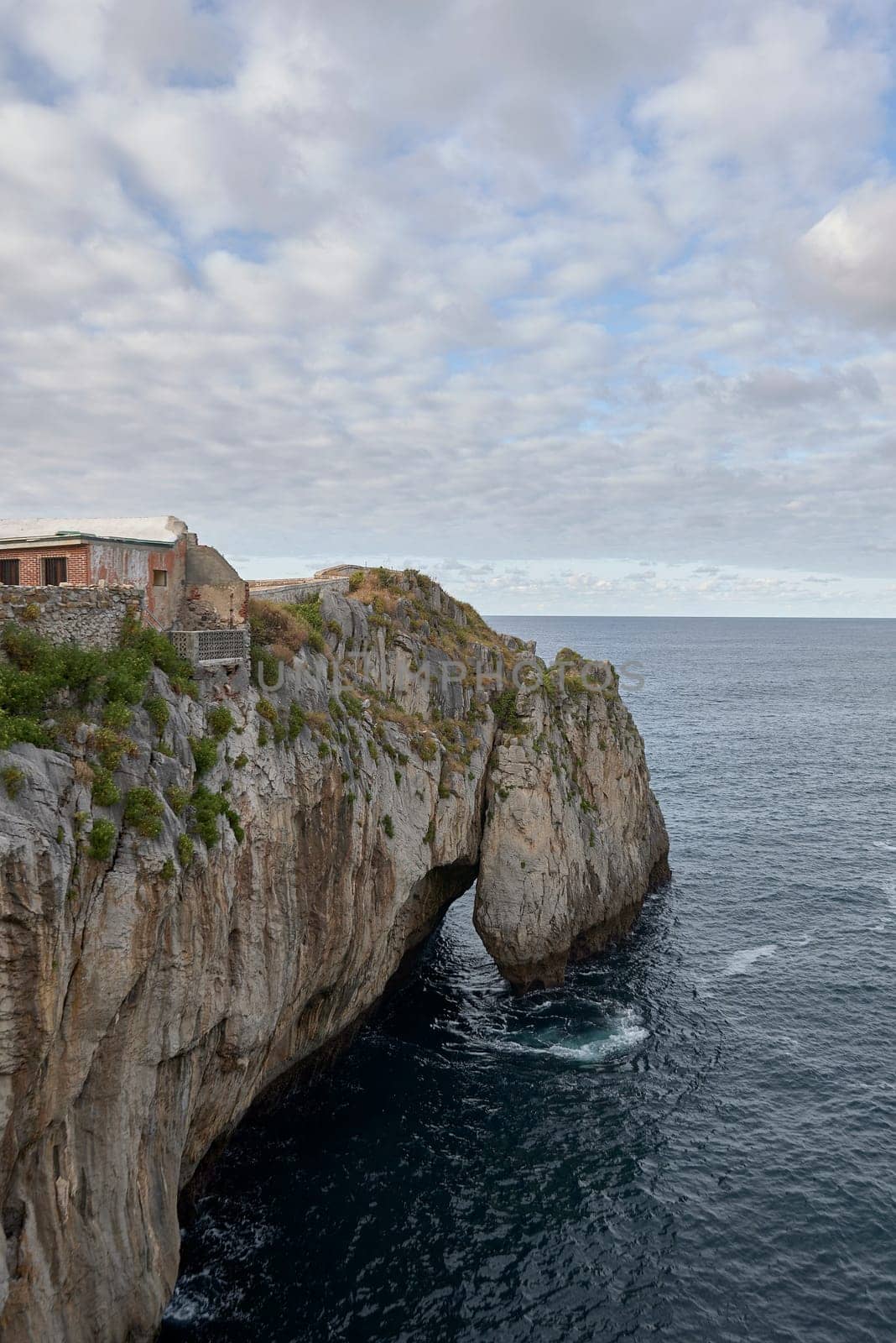 Cliffs on the coast of Castro Urdiales, Spain. Height, calm sea, waves, moving clouds, hole, arc, stone buildings etc