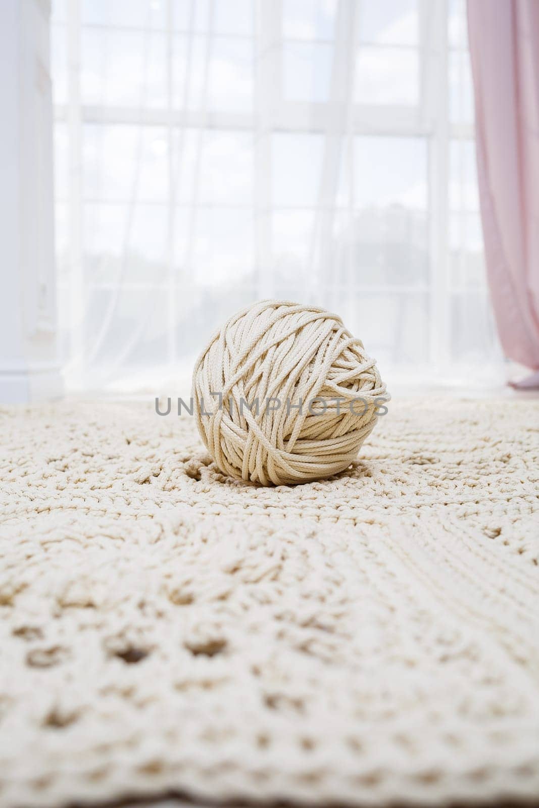 Handmade carpet knitted from natural threads, flooring, natural cotton. Beige handmade carpet. Knitted decorative item. Skein of beige thread for knitting