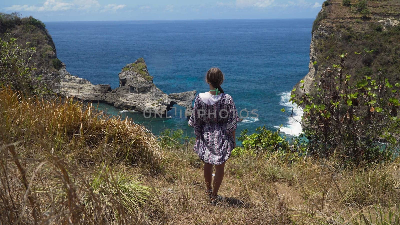 Young girl stands on the edge of a cliff and looks at the sea. Girl on the edge of the cliff enjoys the view of the ocean. Atuh beach on Nusa Penida island. Travel concept.