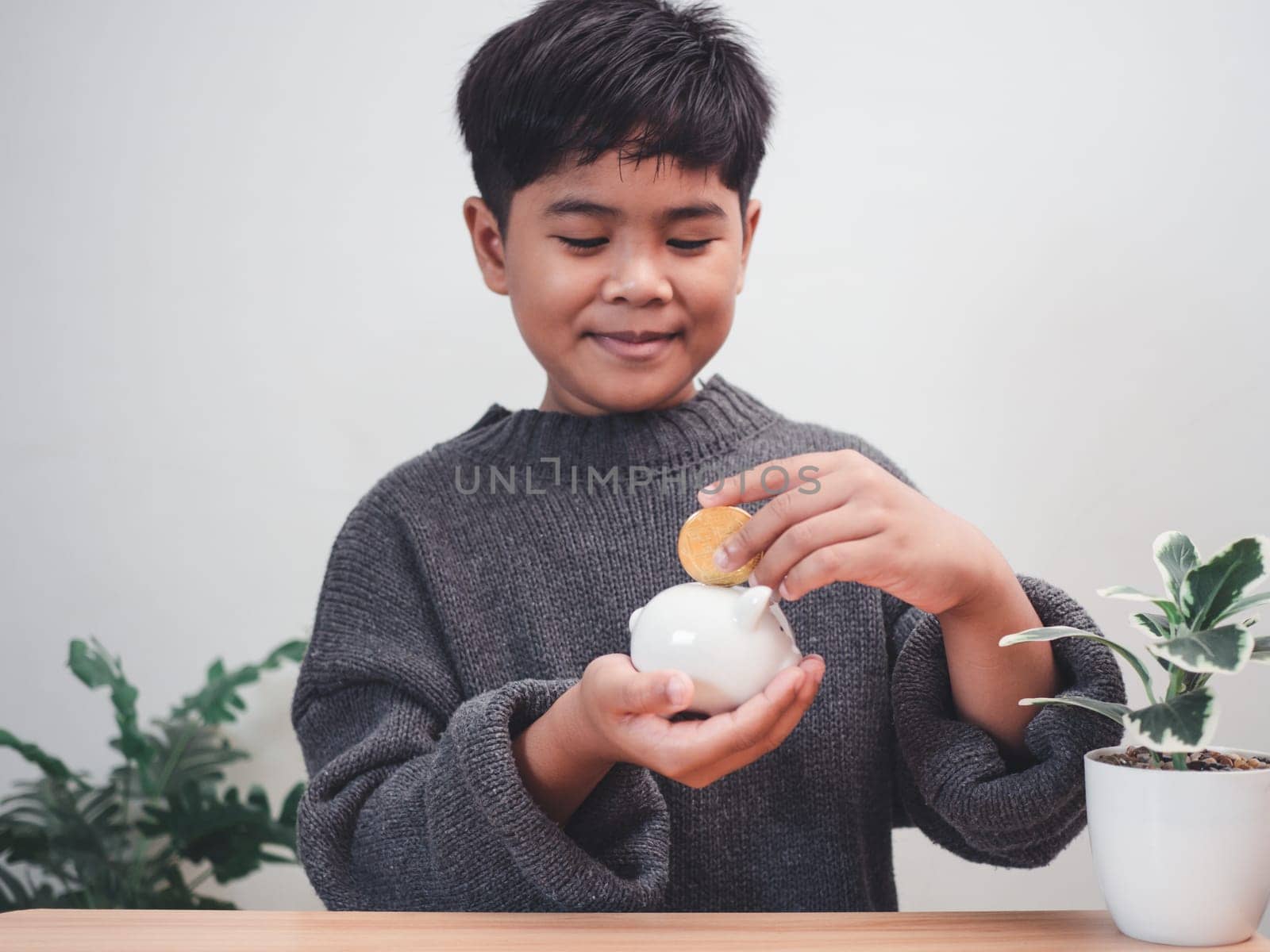 A boy putting coins into piggy bank. Learning financial responsibility and projecting savings. savings concept. investment concept. by Unimages2527