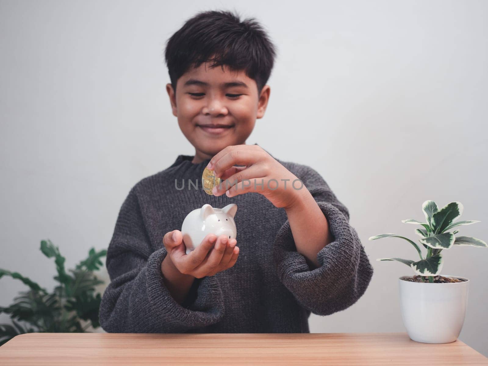 A boy putting coins into piggy bank. Learning financial responsibility and projecting savings. savings concept. investment concept. by Unimages2527