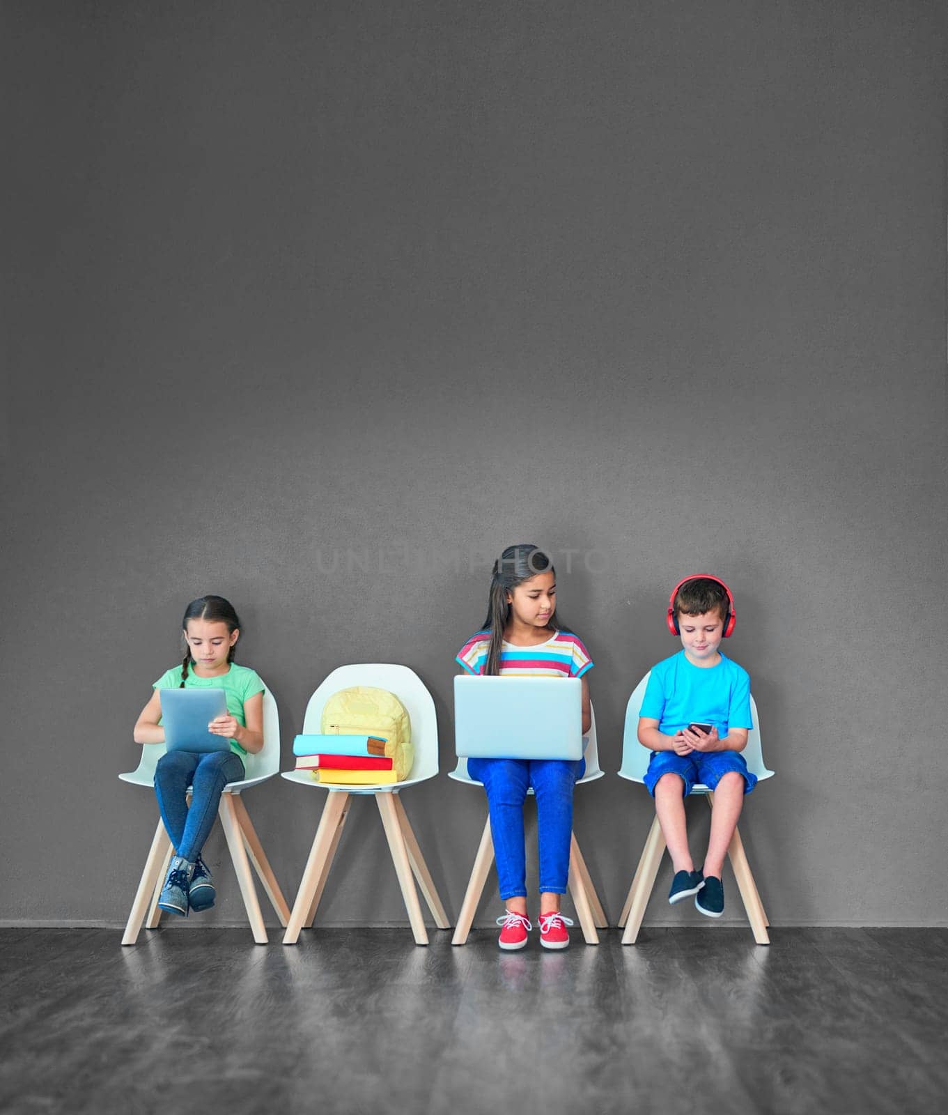 Growing up with wireless gadgets. Studio shot of kids sitting on chairs and using wireless technology against a gray background. by YuriArcurs