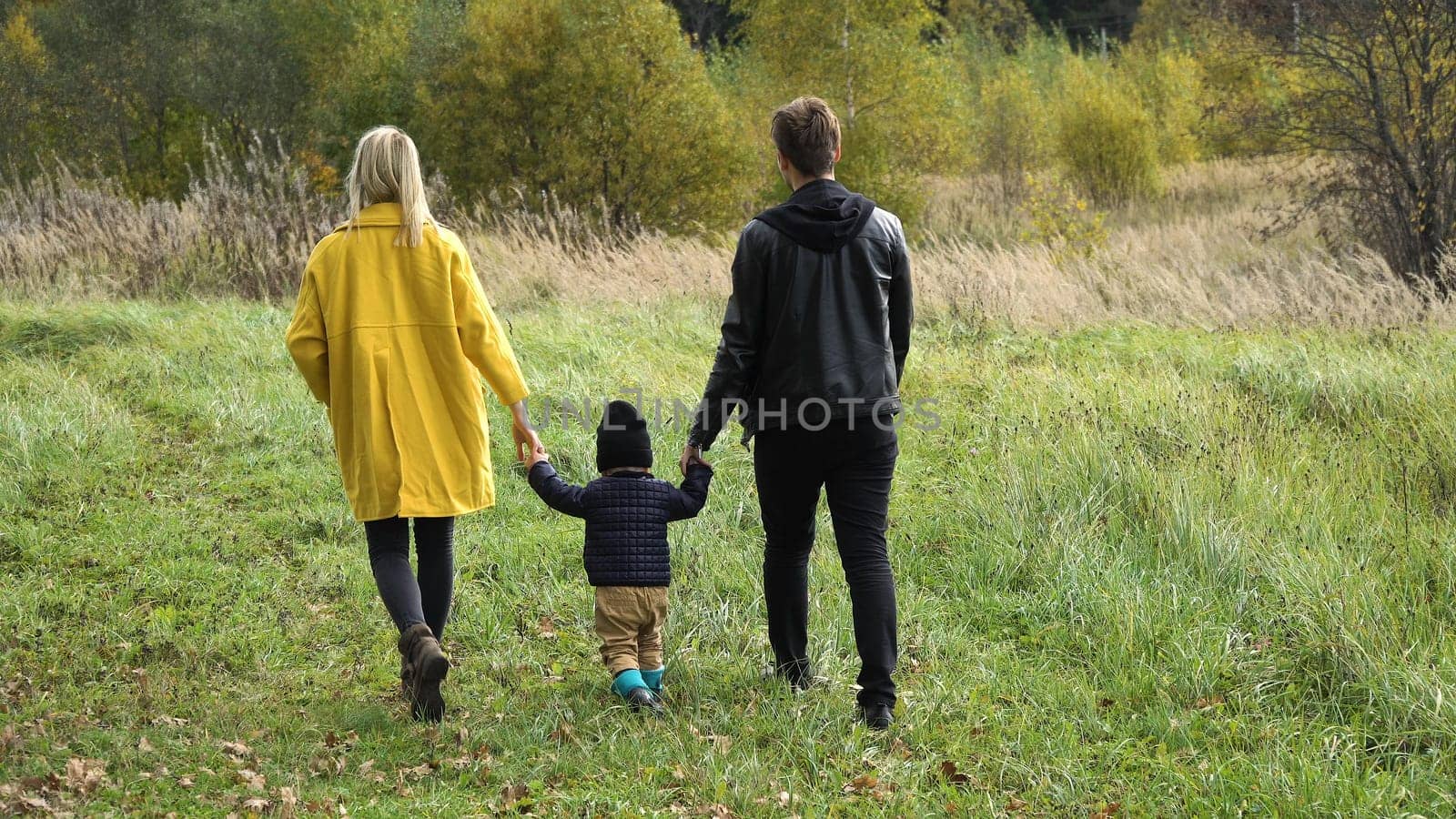 Young family walking in the autumn park with his son, holding his hand.Happy mother, father and little girl walking in autumn park and having fun. Happy young family spending time together outside in green nature.