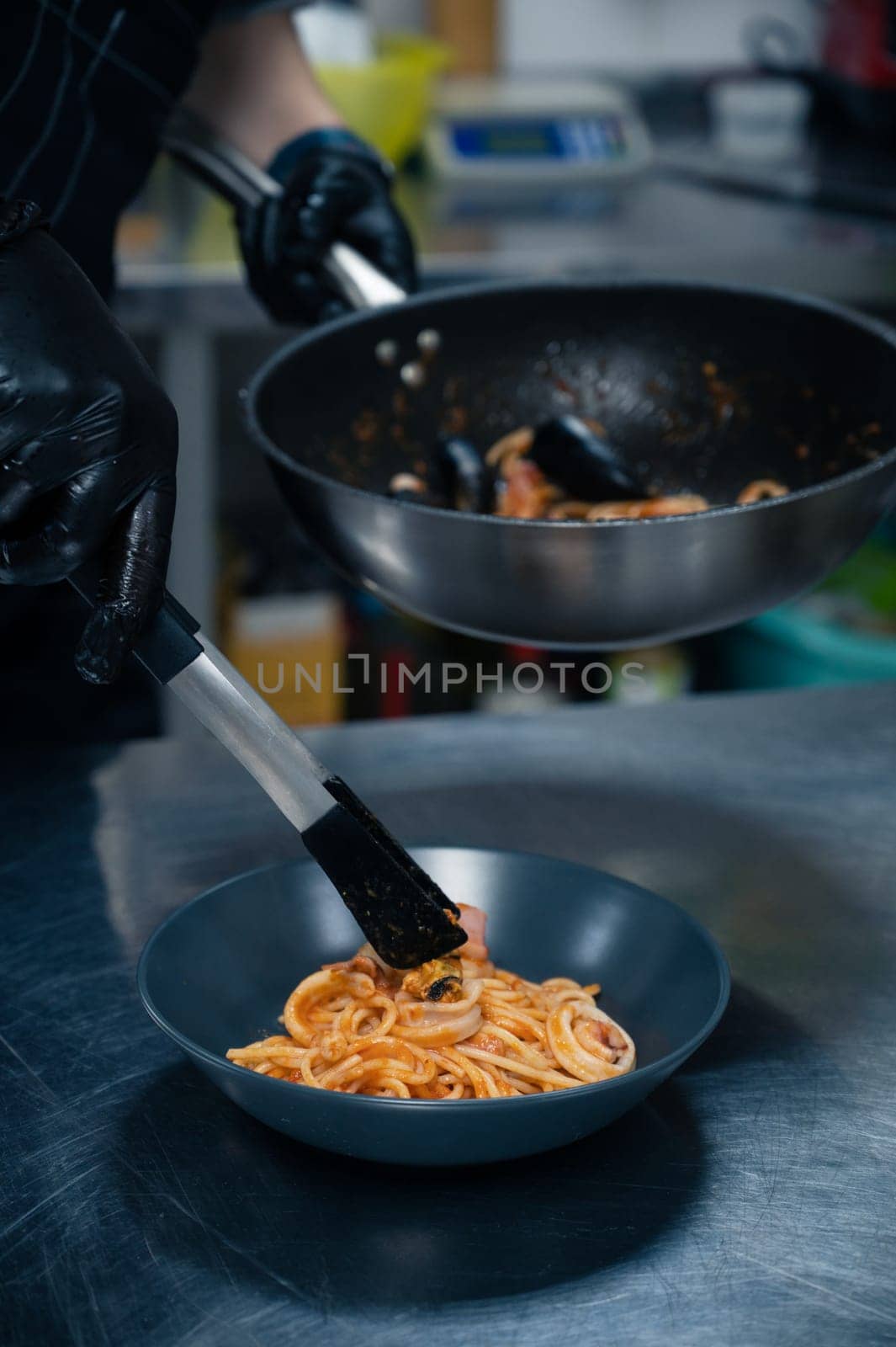 Chef preparing Seafood Pasta with mussels with basil and tomato in black plate