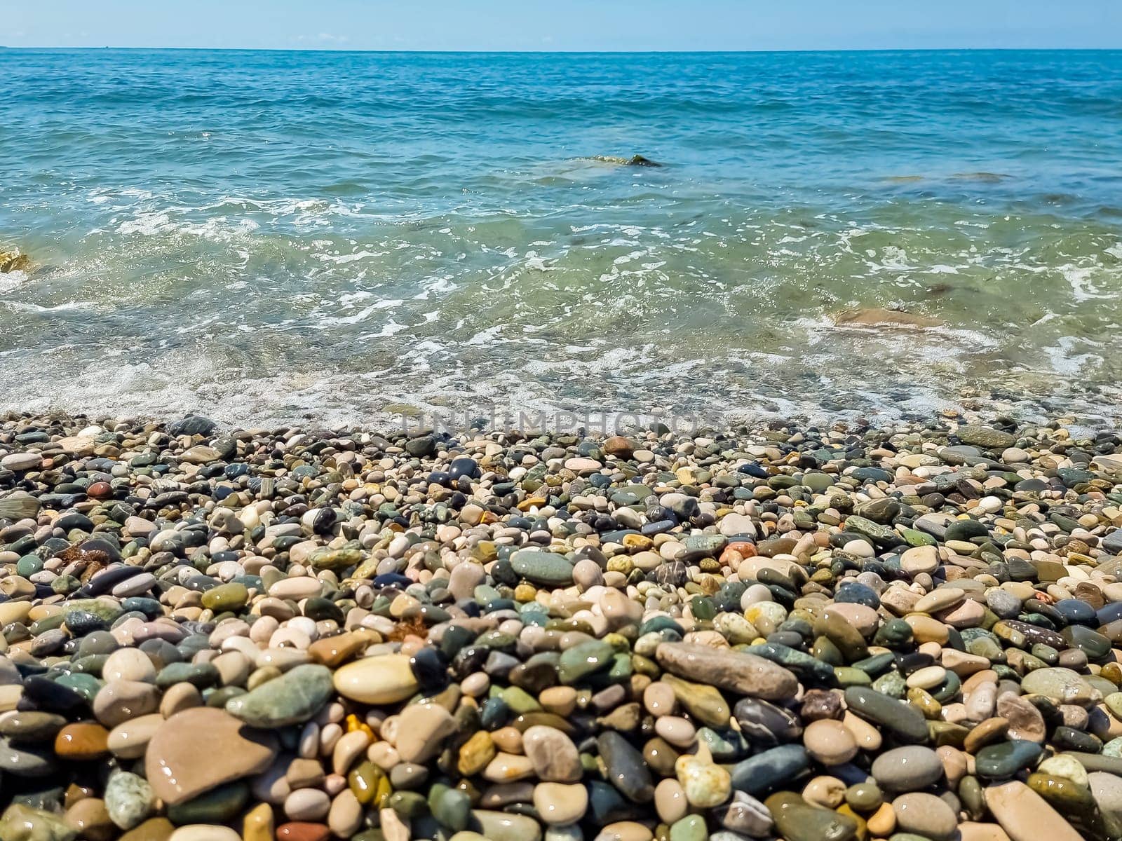 Scenic view of empty pebble sea coast during sunny day