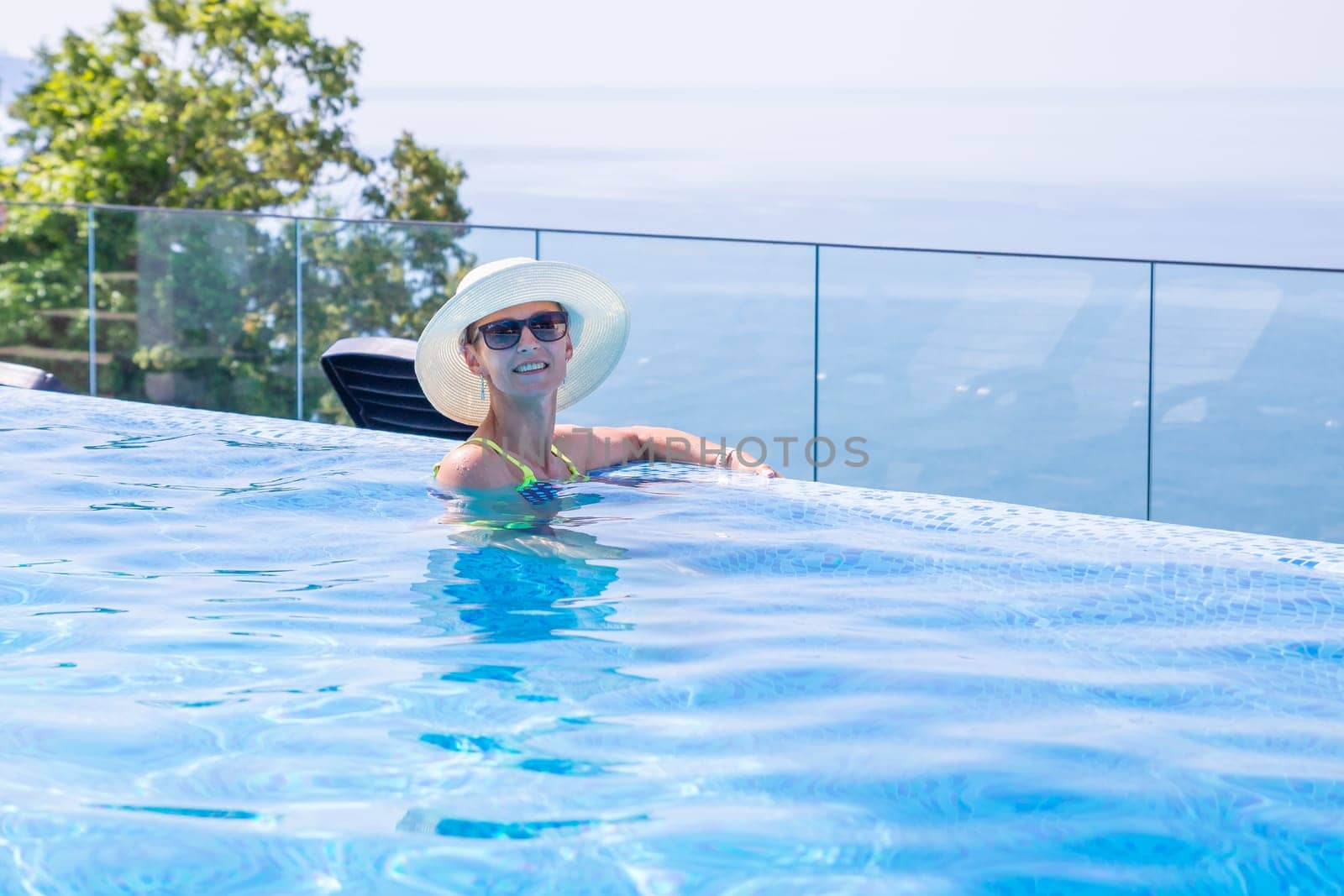 Summer travel vacation concept, Happy traveler asian woman with hat and bikini relax in luxury infinity pool