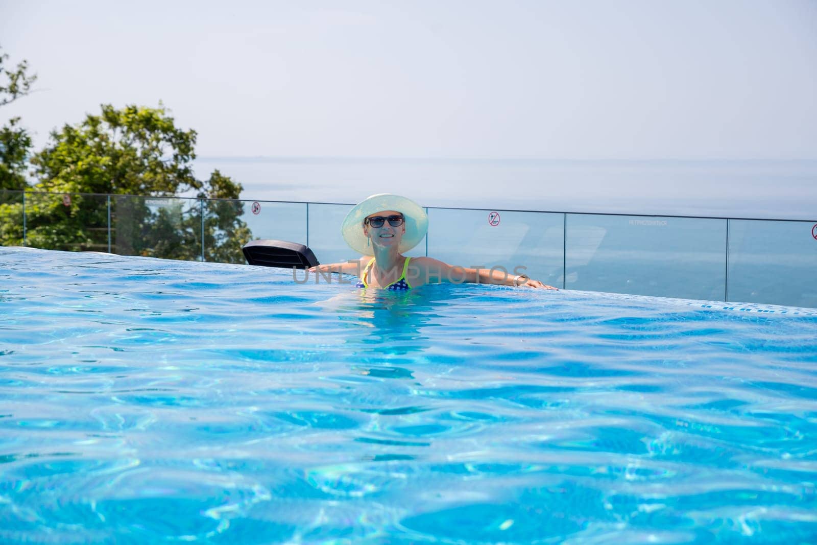 Summer travel vacation concept, Happy traveler asian woman with hat and bikini relax in luxury infinity pool