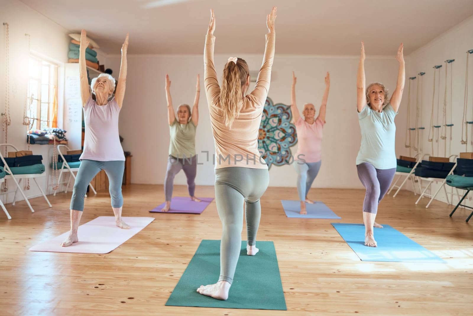 Yoga, exercise and senior class with a fitness instructor or coach in a studio with old people doing exercise, workout and training for wellness in retirement. Women doing warrior pose at health club.