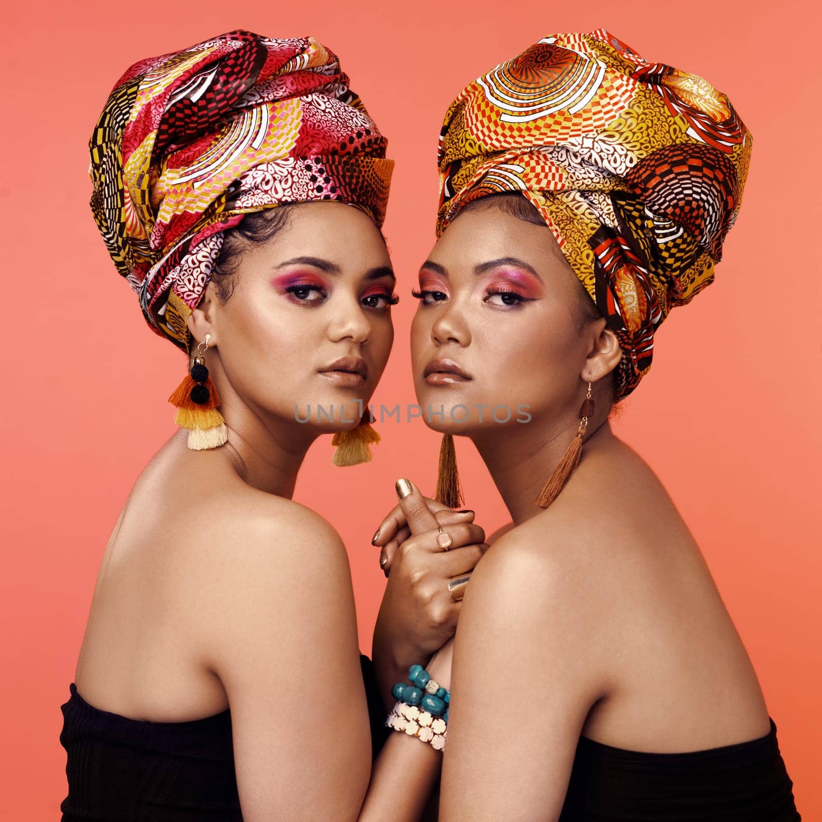 African fashion, makeup and portrait of women on orange background with accessory, makeup and beauty. Glamour, luxury and female people in exotic jewelry, traditional style and head scarf in studio.