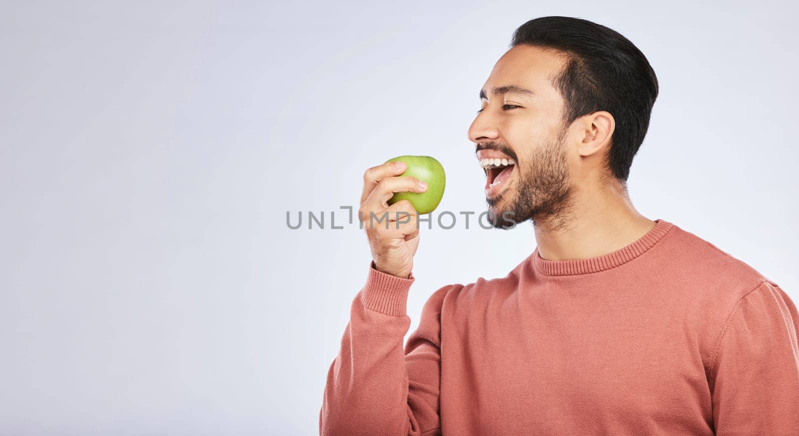 Green apple, eating and happy man isolated on a white background for healthy food, diet and detox space. Vegan person, nutritionist or asian model with fruit for self care or lose weight in studio by YuriArcurs