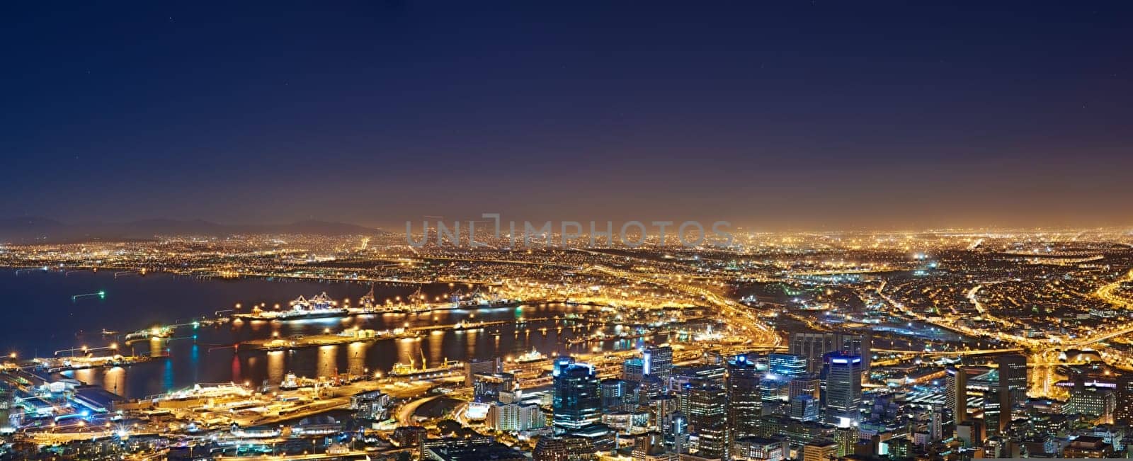 Lights, buildings and drone of the city at night with urban development, sea water and streets. Dark, travel and aerial view of outdoor residential architecture of downtown with a harbour in evening