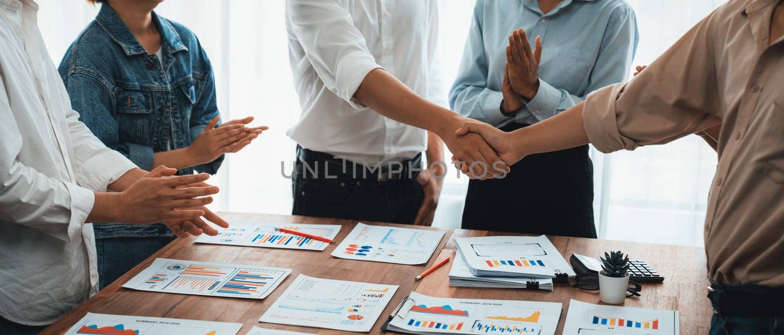 Analyst team celebrates successful data analysis with handshake. Panorama shot handshaking after adjusting attitude or brainstorm for future success in meeting room with BI dashboard paper. Scrutinize
