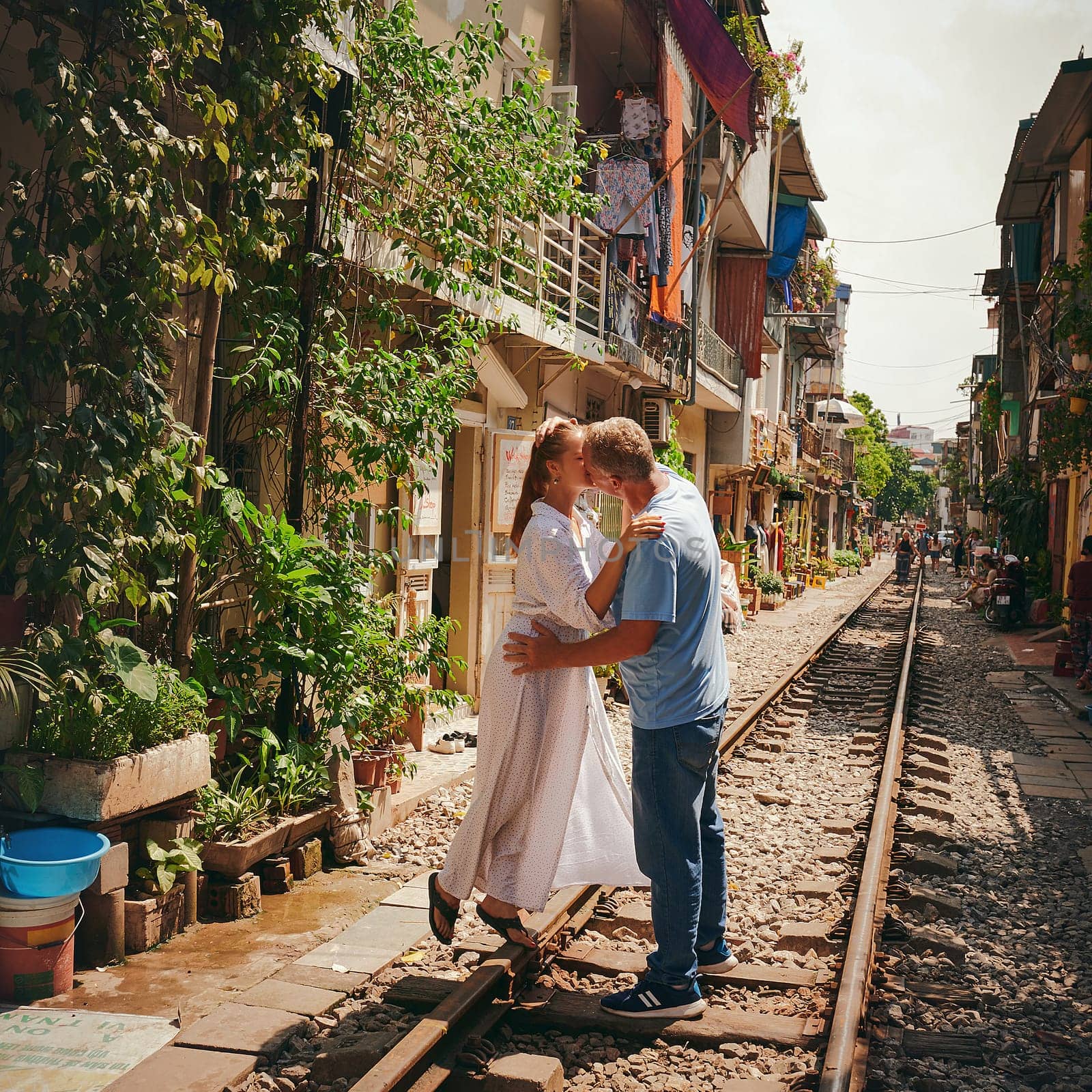 Theres always time for a kiss. a happy couple sharing a romantic moment on the train tracks in the streets of Vietnam. by YuriArcurs