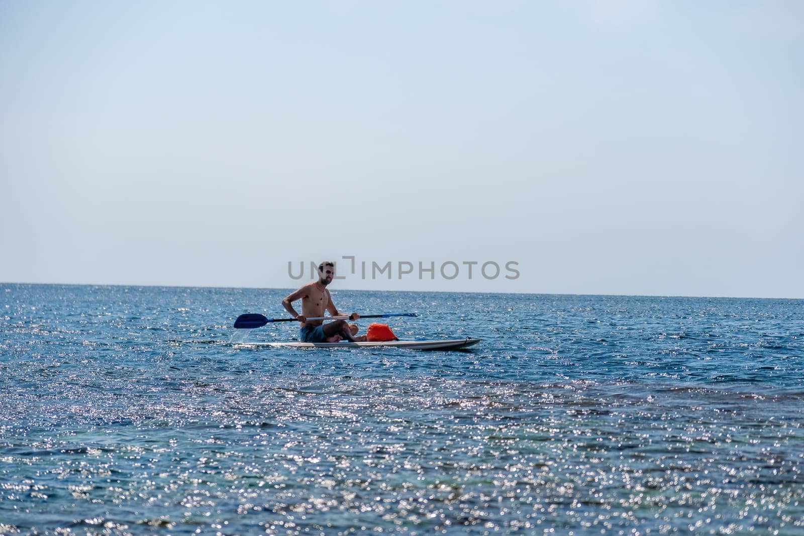 Side view foto of a man swiming and relaxing on the sup board. Sportive man in the sea on the Stand Up Paddle Board SUP. The concept of an active and healthy life in harmony with nature. by panophotograph