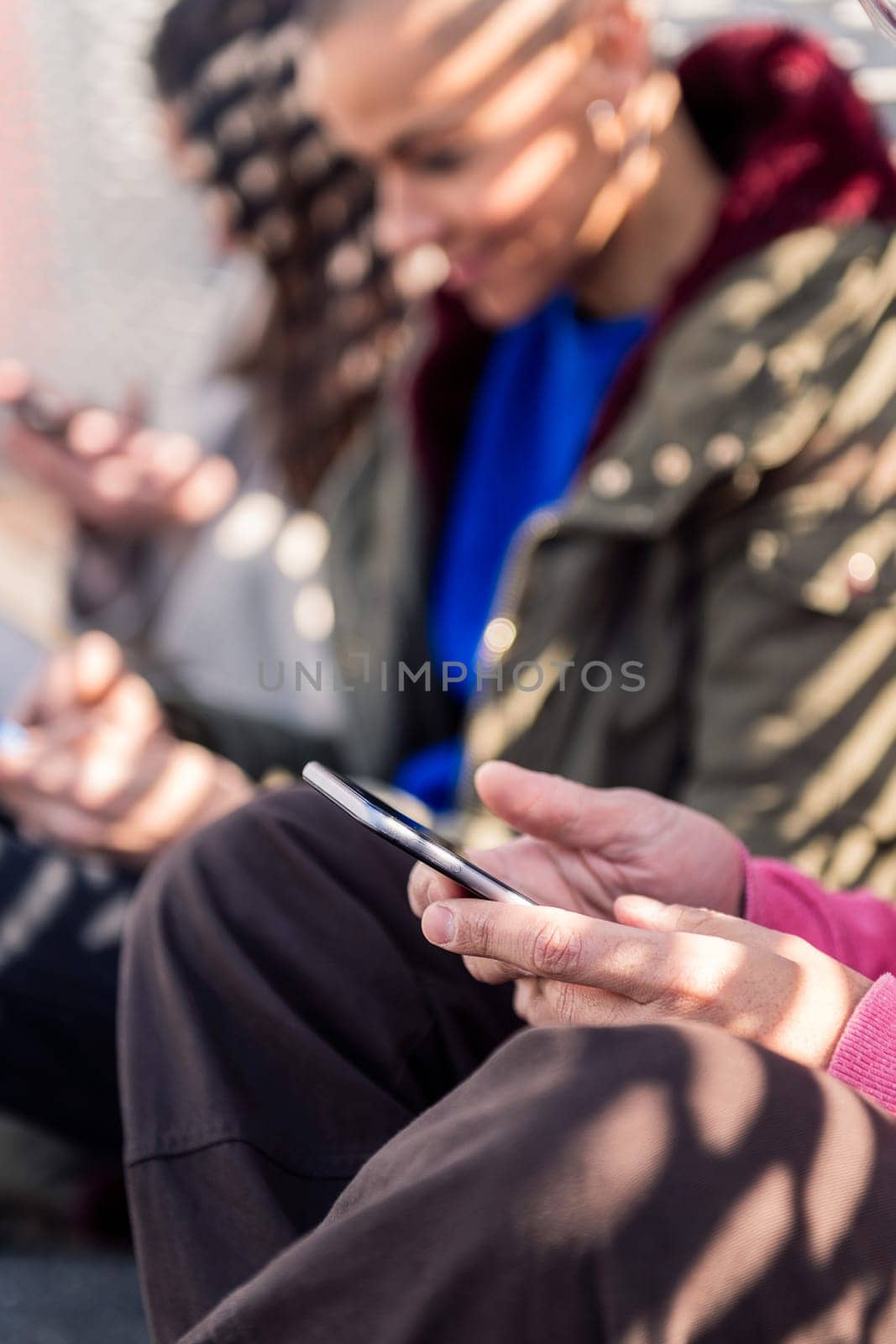 close up of an unrecognizable young man using mobile phone with friends, focus on the hands, concept of technology of communication and modern lifestyle, copy space for text