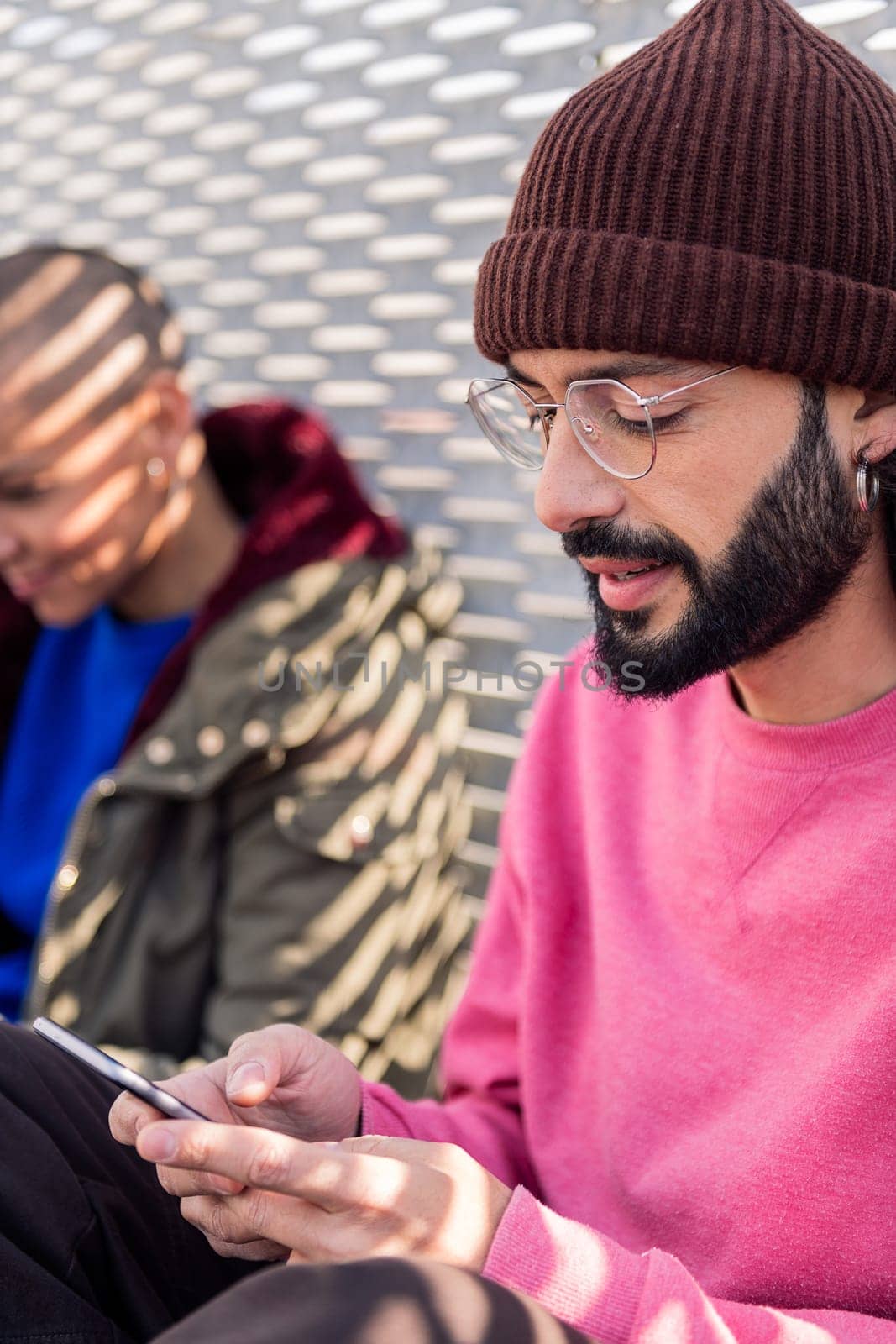 young bearded man using mobile phone with friends sitting in the floor at city, concept of technology of communication and modern lifestyle, copy space for text