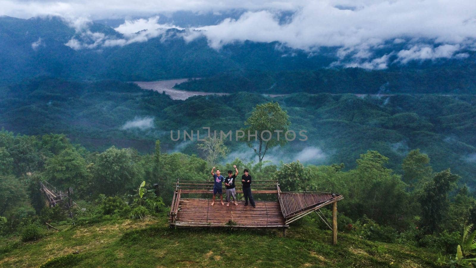 June 24, 2023; Mae Hong Son, Thailand - Group of young tourists taking photos by drone against the landscape of misty valley and cloudy mountains in Thailand.