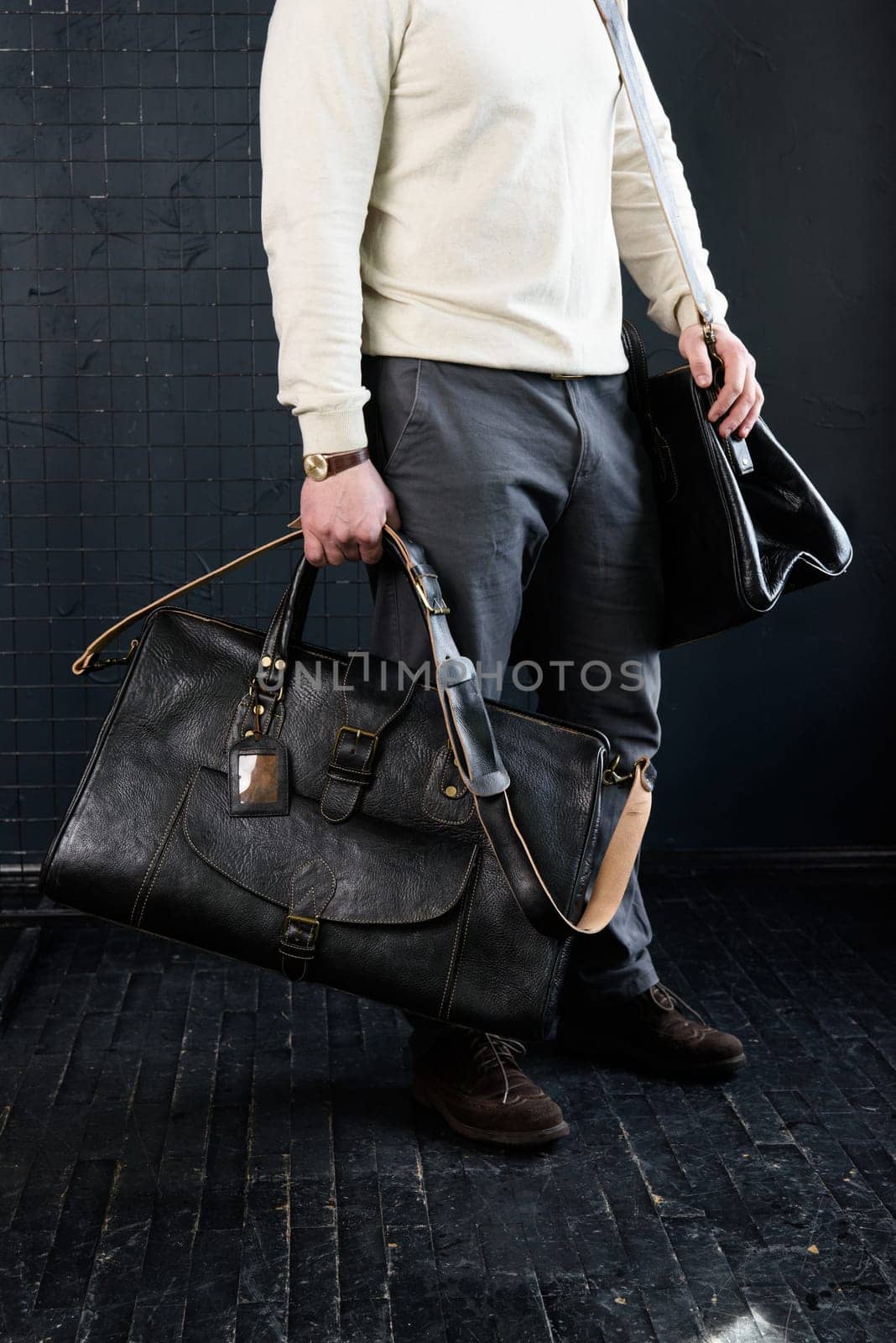 a man with bags. two different size black leather travel bags, indoors photo on black background.