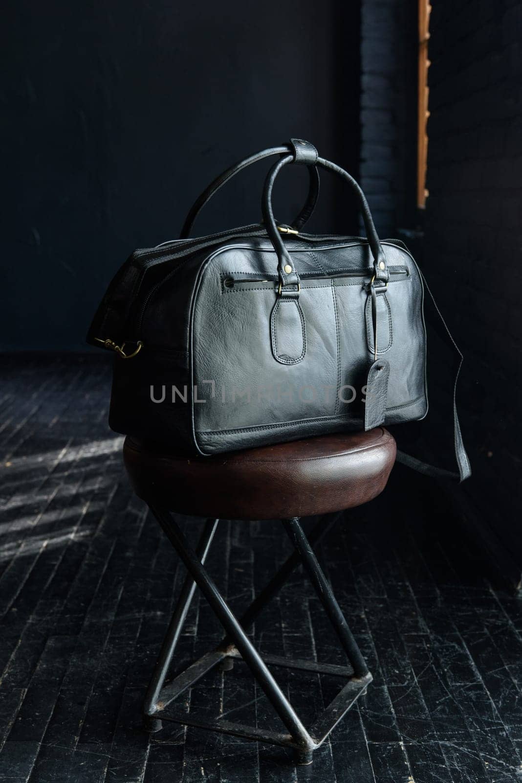 black leather travel bag, indoors photo on black background.