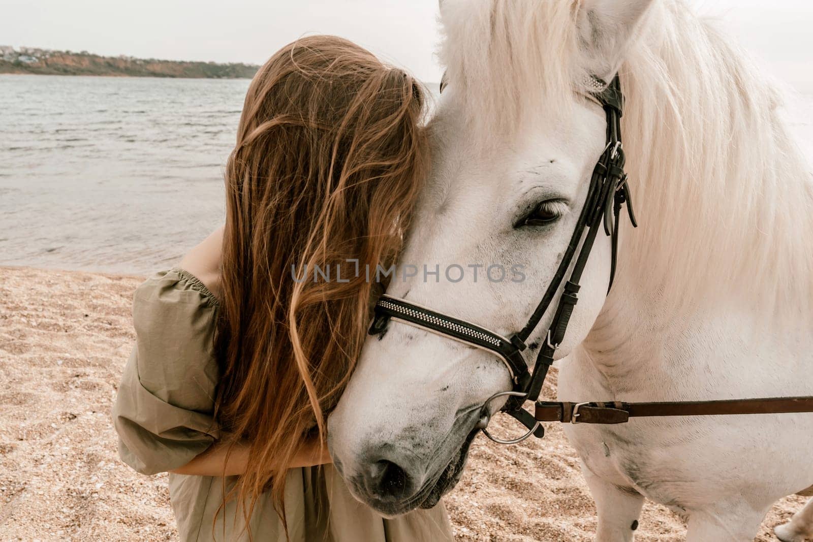 A white horse and a woman in a dress stand on a beach, with the sky and sea creating a picturesque backdrop for the scene