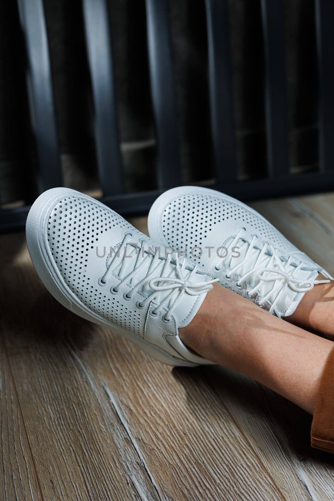 Female legs in white leather sneakers with perforations. Collection of summer women's shoes. White women's sneakers with laces