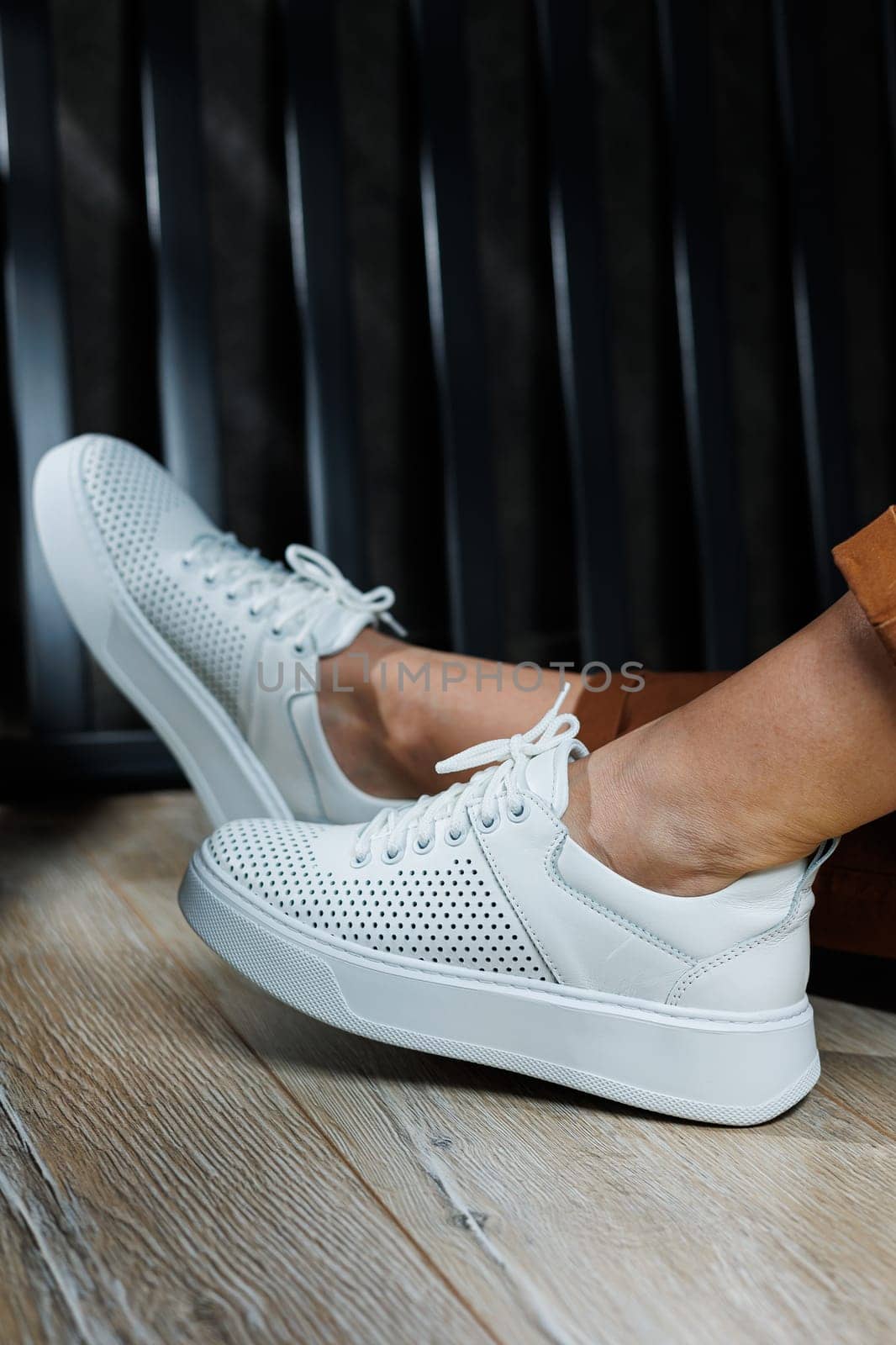 Female legs in white leather sneakers with perforations. Collection of summer women's shoes. White women's sneakers with laces