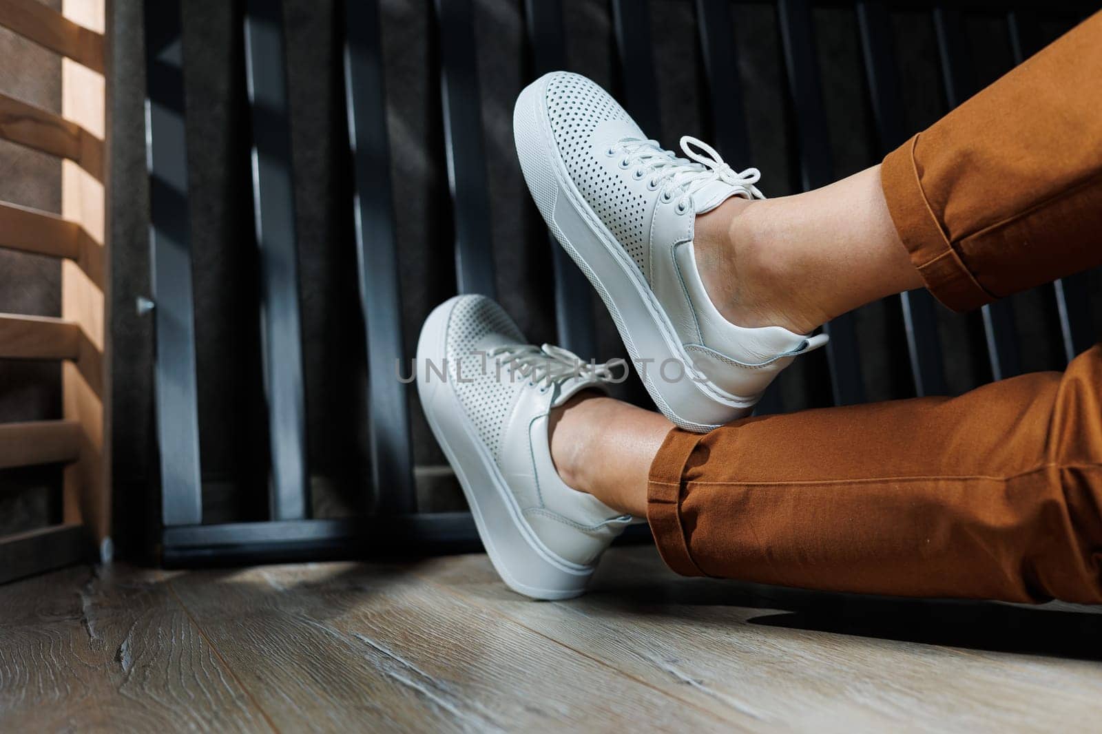 Female legs in white leather sneakers with perforations. Collection of summer women's shoes. White women's sneakers with laces
