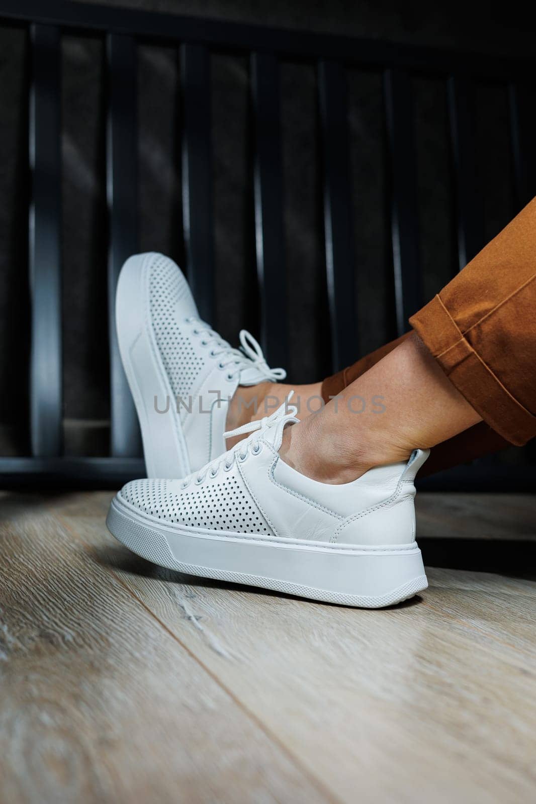 Female legs in white leather sneakers with perforations. Collection of summer women's shoes. White women's sneakers with laces