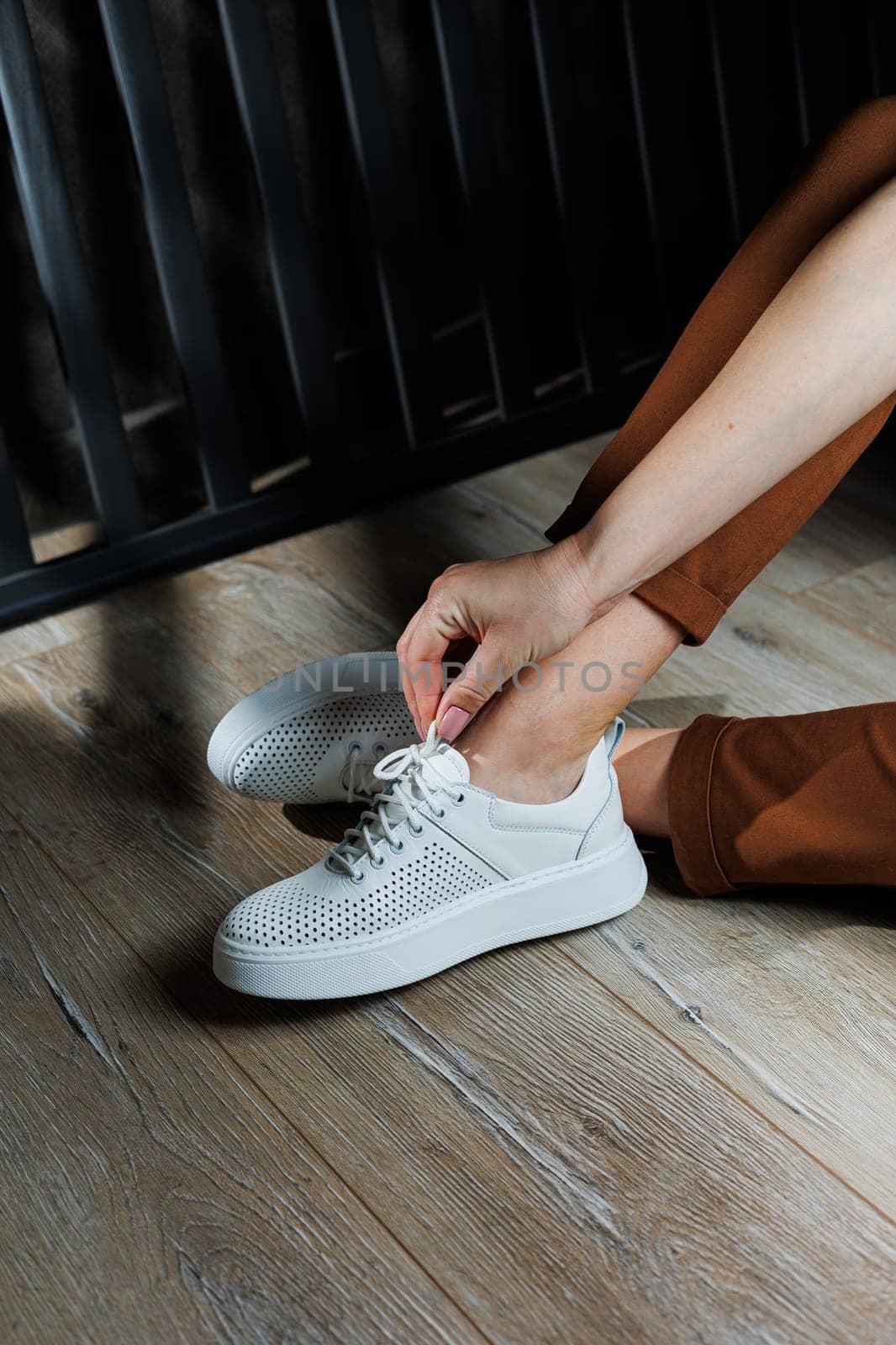 Female legs in white leather sneakers with perforations. Collection of summer women's shoes. White women's sneakers with laces