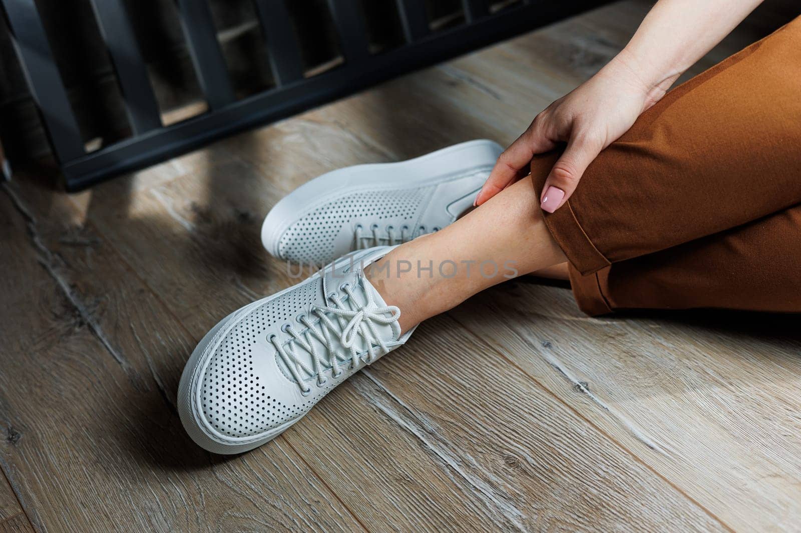 Female legs in white leather sneakers with perforations. Collection of summer women's shoes. White women's sneakers with laces