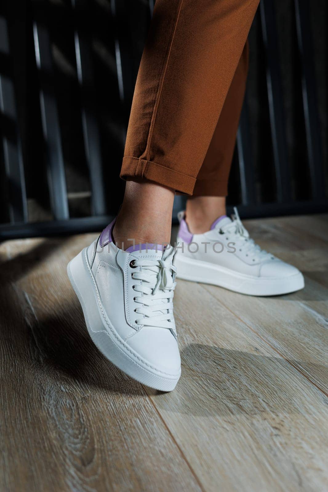 Female legs in white leather sneakers with perforations. Collection of summer women's shoes. White women's sneakers with laces