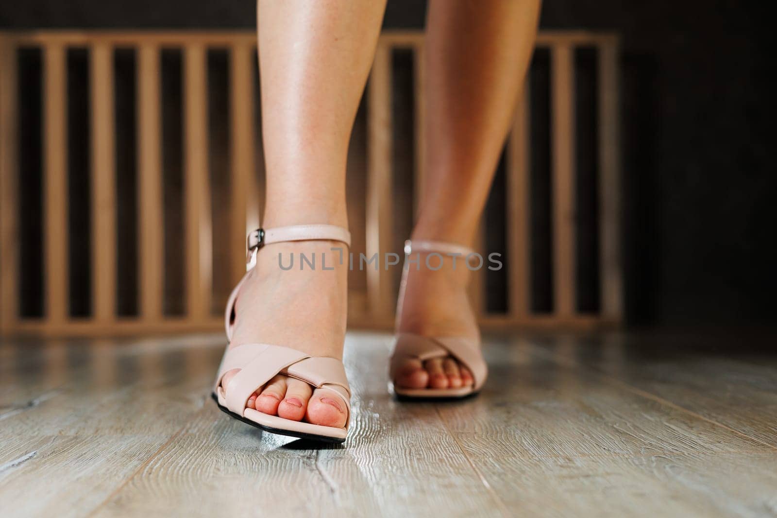 Beautiful slender legs of a girl in leather sandals on high heels on the floor against gray parquet. Collection of women's sandals