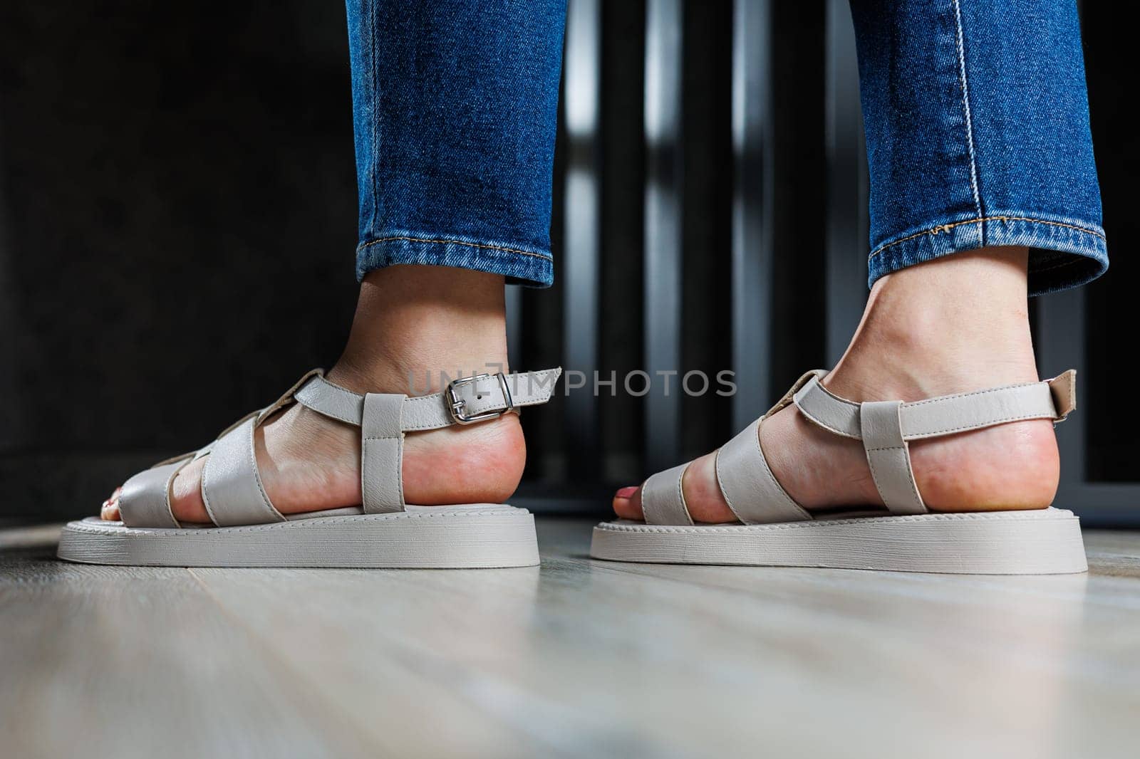 Beautiful slender female legs in leather sandals on the floor against gray parquet. Collection of women's sandals by Dmitrytph