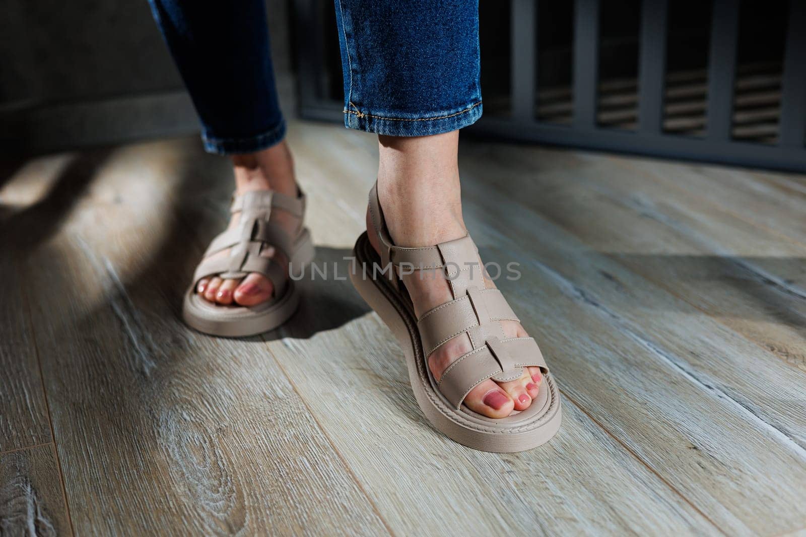 Collection of women's leather summer sandals. Slender female legs in beige leather sandals without heels.