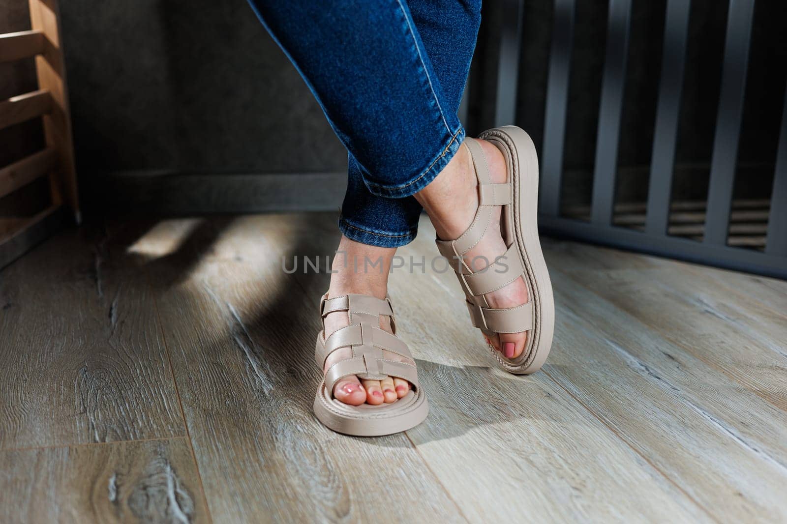Collection of women's leather summer sandals. Slender female legs in beige leather sandals without heels.