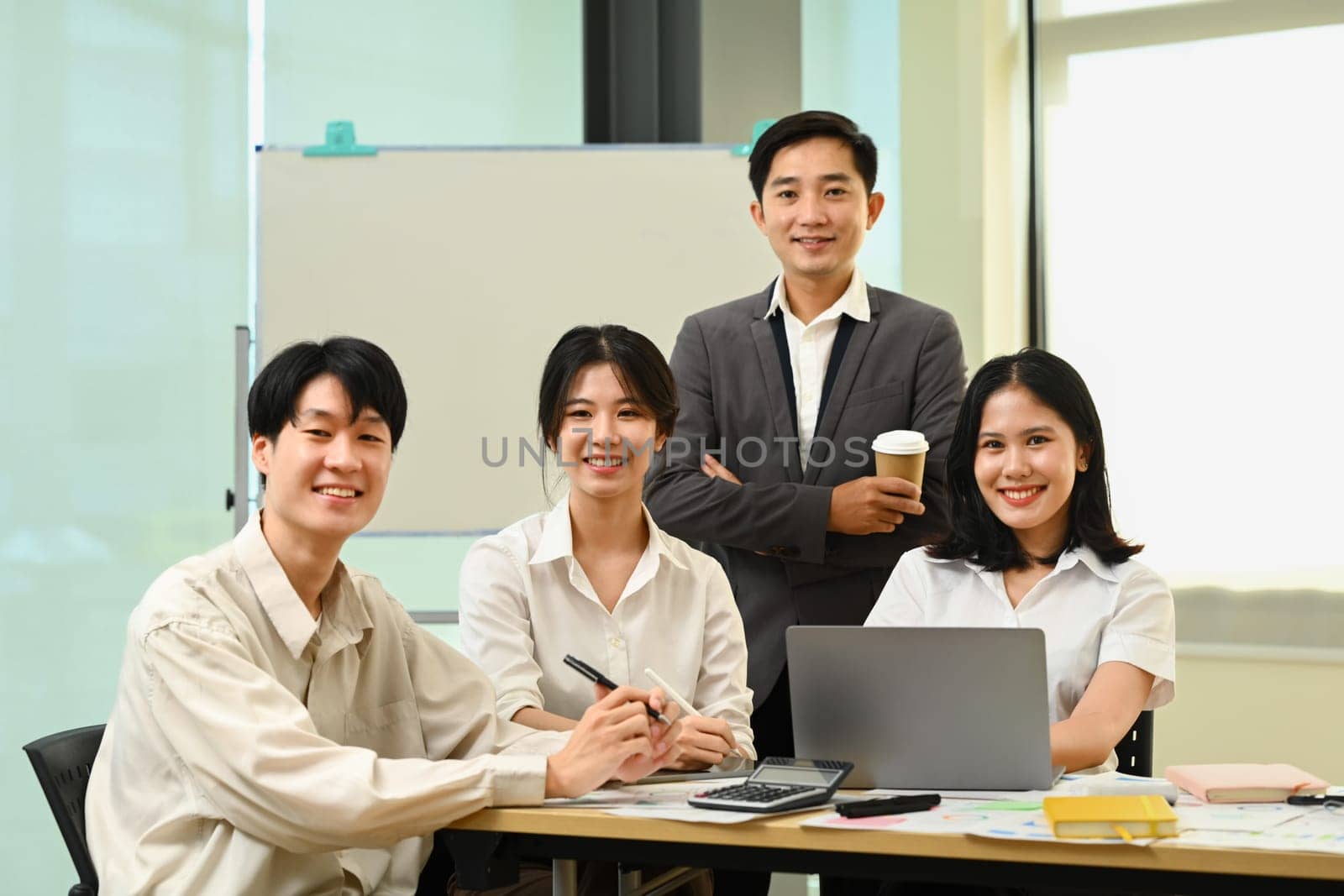 Group of company employees sitting in modern office and smiling confidently to camera.