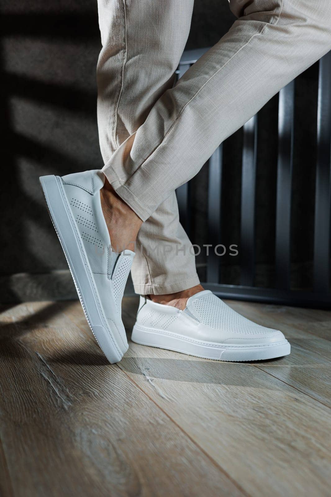 Close-up of male feet in white casual shoes. Fashionable young man standing in leather stylish white moccasins in fashionable trousers. Seasonal summer men's shoes. Casual street style.