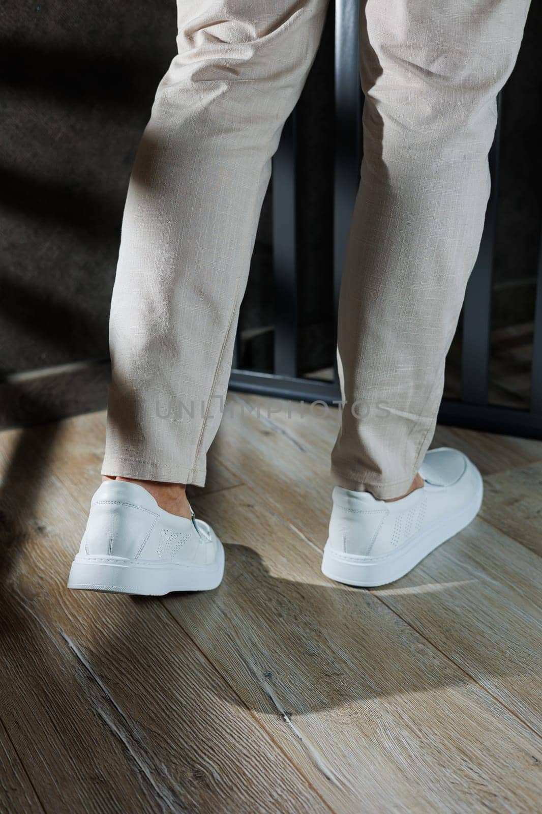 Close-up of male feet in white casual shoes. Fashionable young man standing in leather stylish white moccasins in fashionable trousers. Seasonal summer men's shoes. Casual street style.