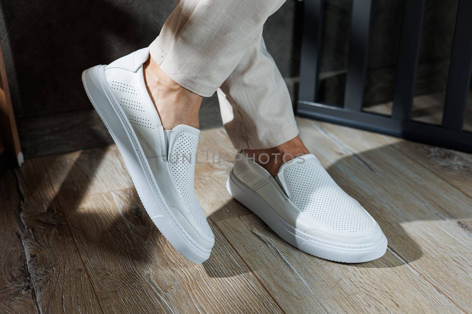 Close-up of male feet in white casual shoes. Fashionable young man standing in leather stylish white moccasins in fashionable trousers. Seasonal summer men's shoes. Casual street style.