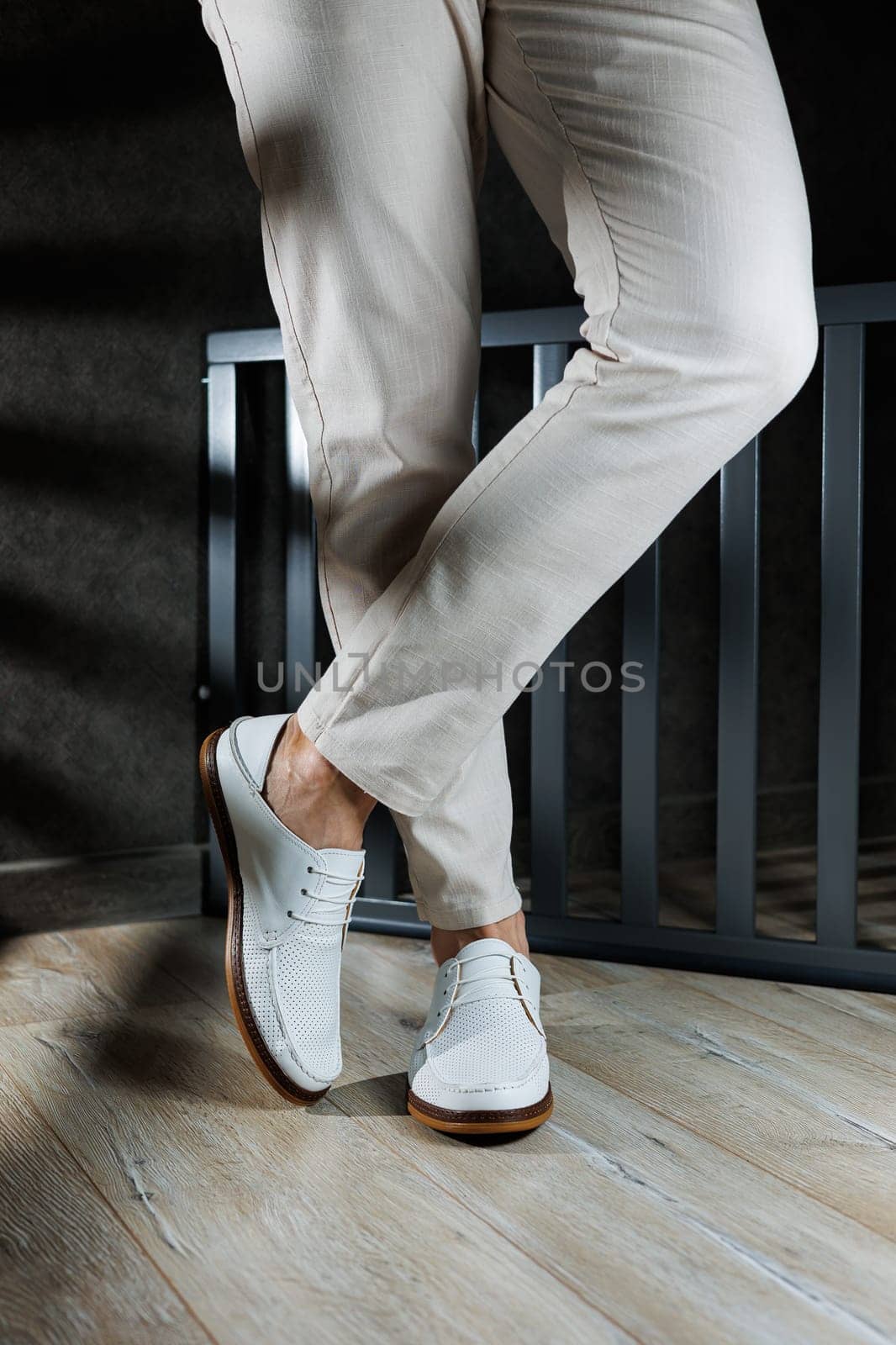 Male feet close-up in white casual shoes. Fashionable young man standing in leather stylish white moccasins in trousers. Seasonal summer men's shoes. Casual street style.