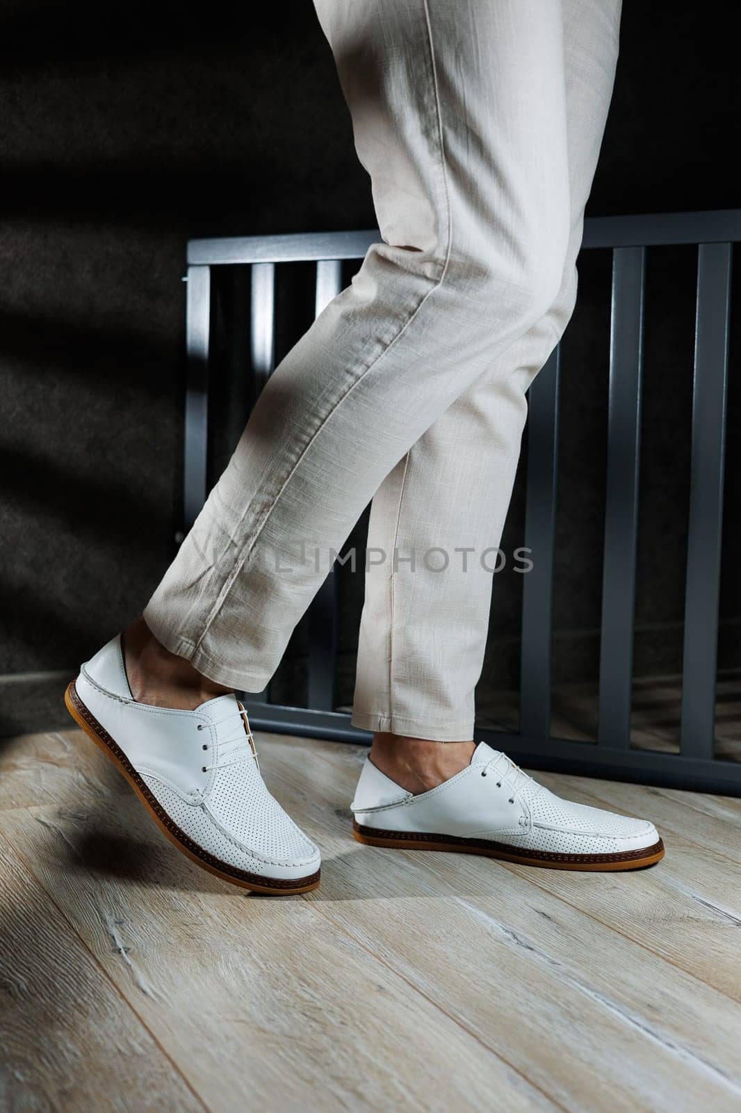 Male feet close-up in white casual shoes. Fashionable young man standing in leather stylish white moccasins in trousers. Seasonal summer men's shoes. Casual street style.