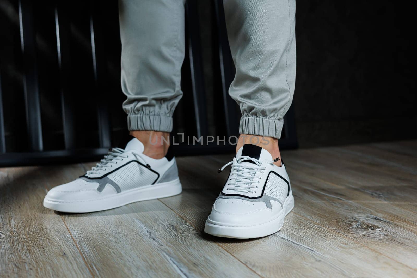 Male legs in white leather summer shoes. Comfortable men's white sneakers with laces. Casual men's sneakers