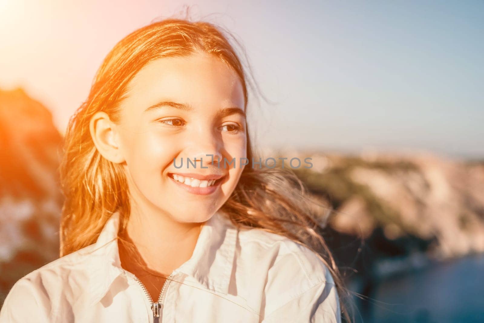 Brown-haired young romantic teenager girl corrects long hair on beach at summer evening wind