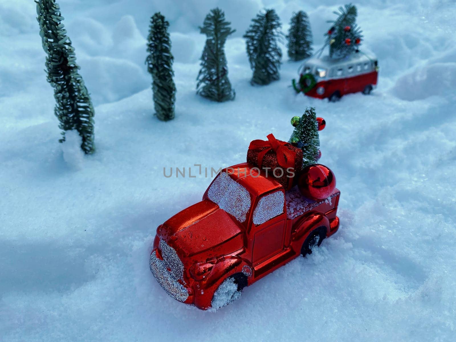 Christmas decorations in the form of red cars are carrying Christmas trees against the backdrop of snow. The concept of Christmas and winter holidays