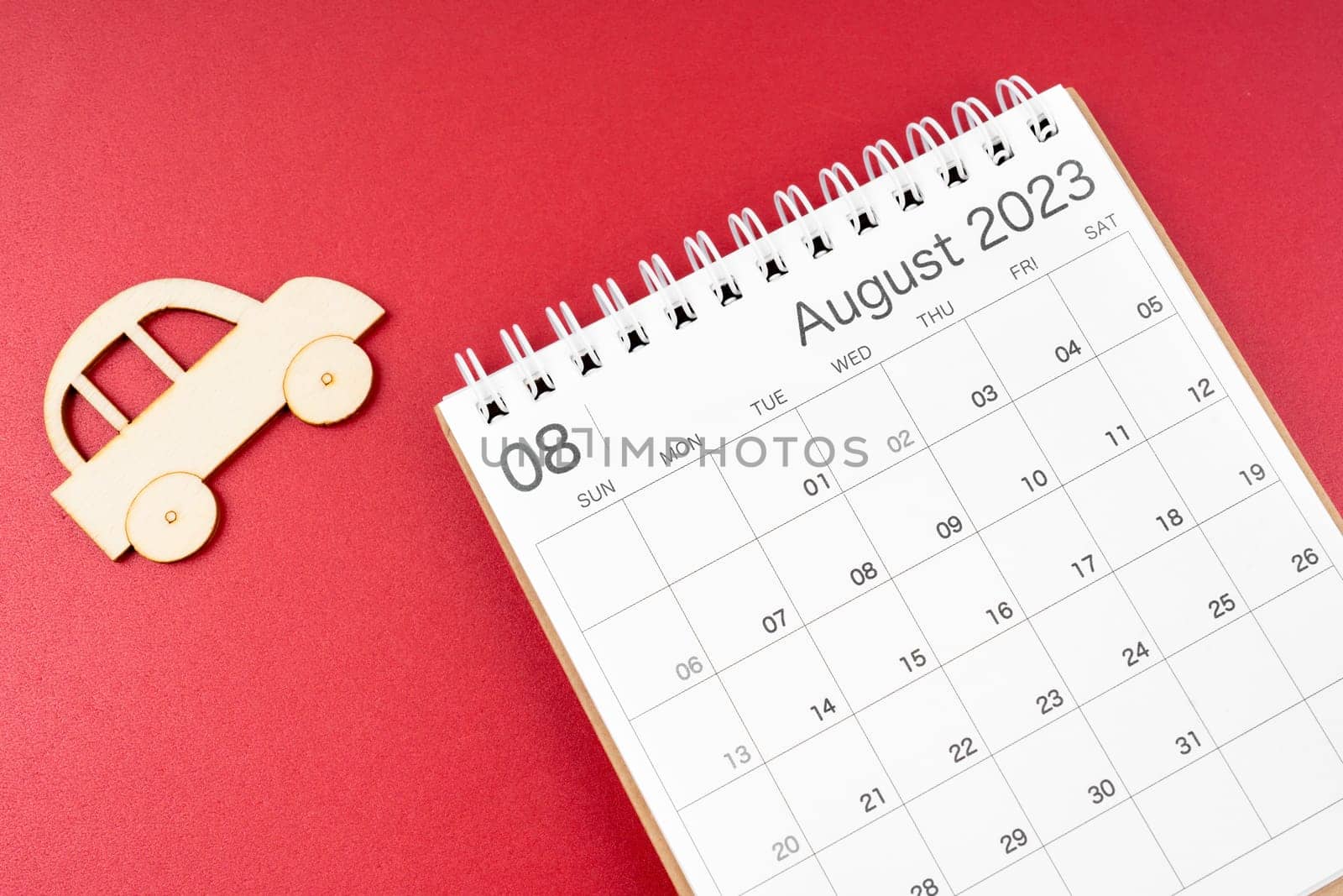 The August 2023 desk calendar and wooden toy cars on red background. by Gamjai