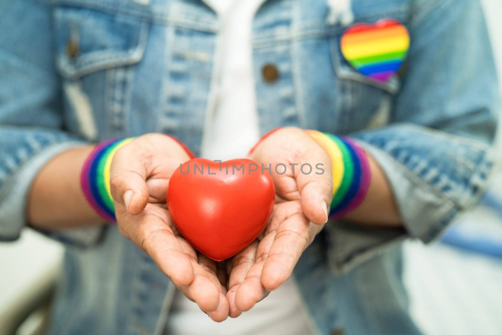 Asian lady wearing rainbow flag wristbands and hold red heart, symbol of LGBT pride month celebrate annual in June social of gay, lesbian, bisexual, transgender, human rights. by pamai